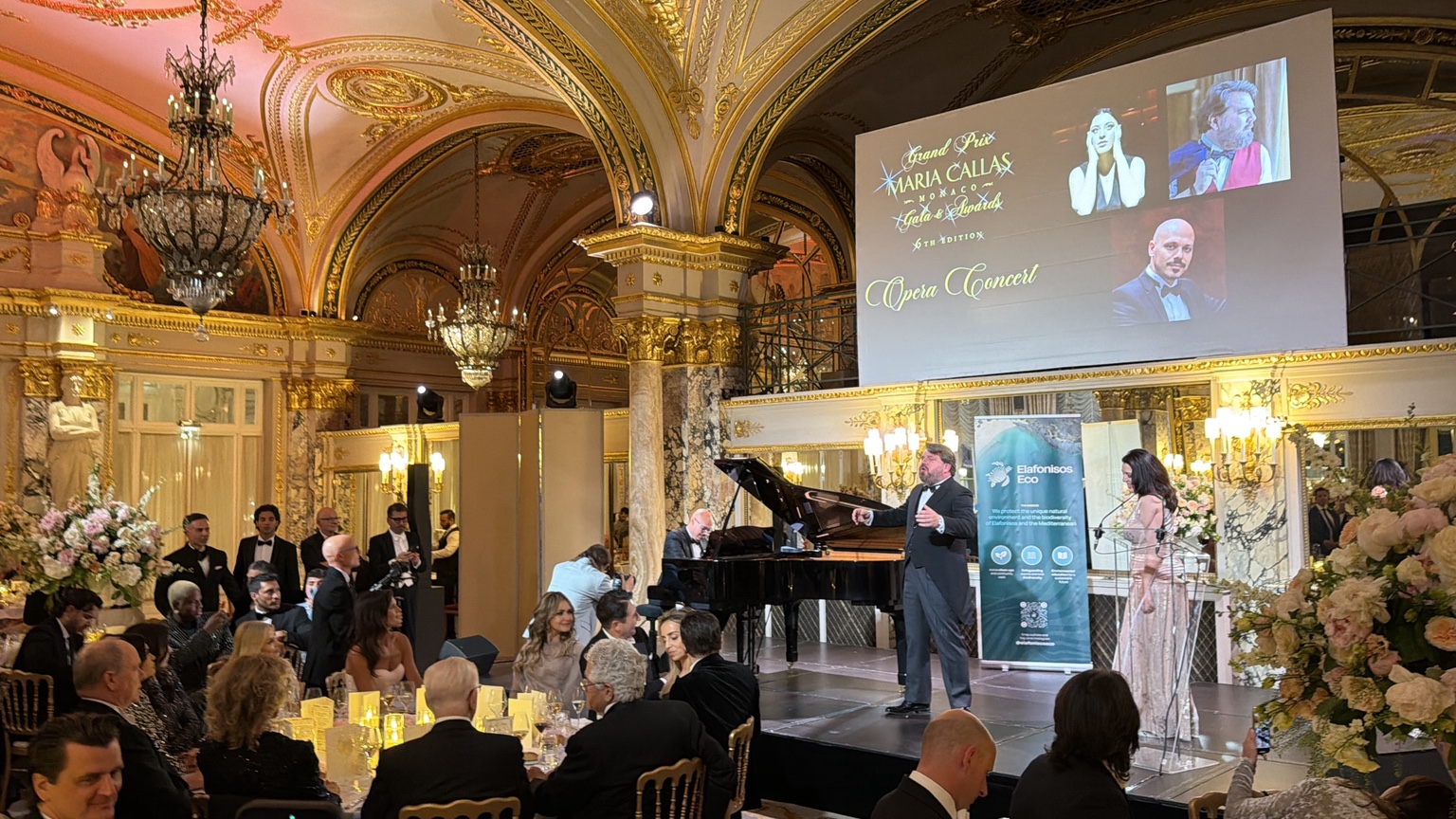 Opera performers and pianist on the Salle Empire stage, with the sixth-edition event screen